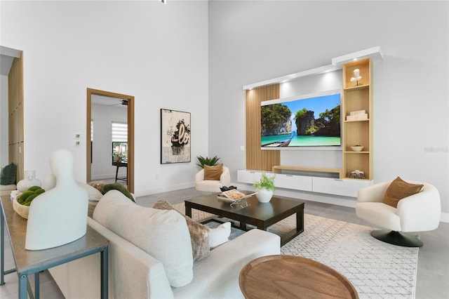 living room with ceiling fan, built in features, and a towering ceiling