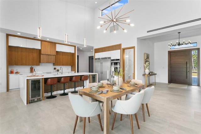 dining area with sink, a chandelier, a towering ceiling, and wine cooler