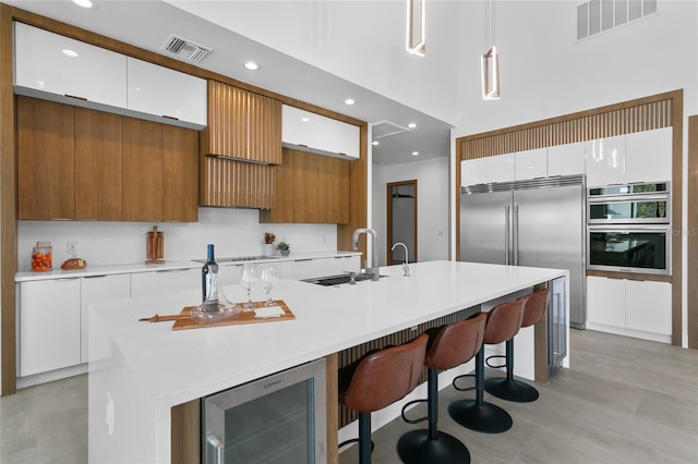 kitchen with decorative light fixtures, beverage cooler, white cabinets, and a kitchen island with sink