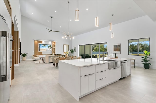 kitchen with hanging light fixtures, a kitchen island with sink, a high ceiling, and white cabinetry