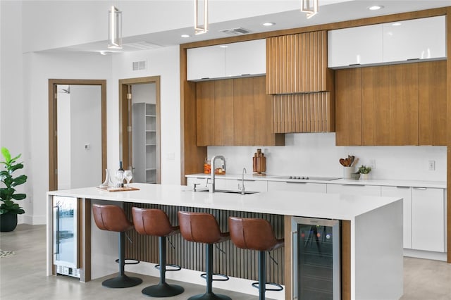 kitchen with wine cooler, white cabinets, an island with sink, and hanging light fixtures