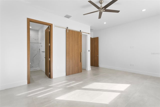 unfurnished bedroom featuring ensuite bath, a barn door, and ceiling fan