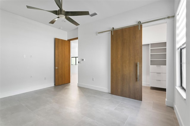 unfurnished bedroom with ceiling fan, a barn door, a closet, and a spacious closet