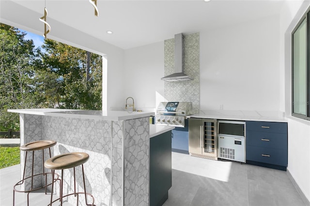 kitchen with high quality fridge, wall chimney exhaust hood, a kitchen bar, tasteful backsplash, and blue cabinetry