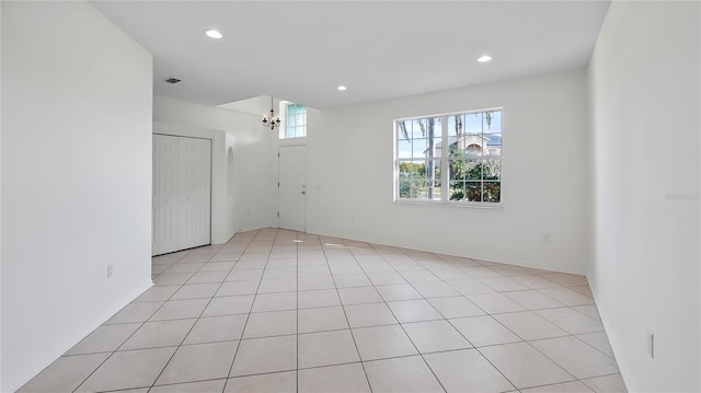 tiled spare room featuring a healthy amount of sunlight and a notable chandelier