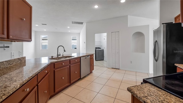 kitchen featuring sink, appliances with stainless steel finishes, light tile patterned flooring, washer / dryer, and dark stone counters