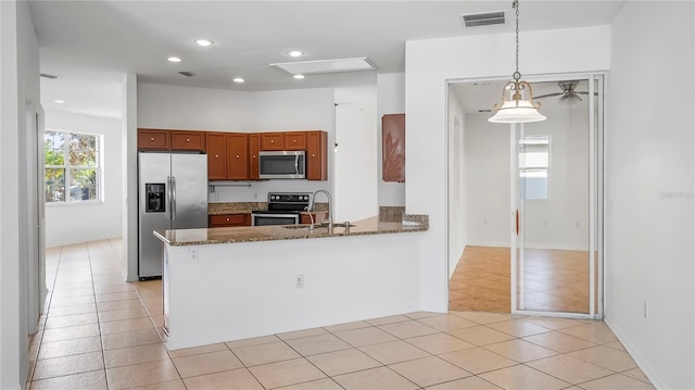 kitchen with sink, appliances with stainless steel finishes, kitchen peninsula, decorative light fixtures, and dark stone counters