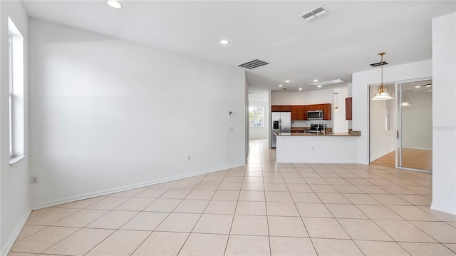 kitchen featuring light tile patterned floors, decorative light fixtures, kitchen peninsula, and appliances with stainless steel finishes