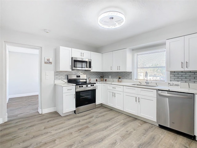 kitchen featuring sink, light hardwood / wood-style flooring, white cabinetry, stainless steel appliances, and decorative backsplash