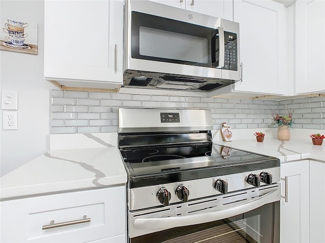 kitchen with light stone countertops, appliances with stainless steel finishes, white cabinets, and backsplash