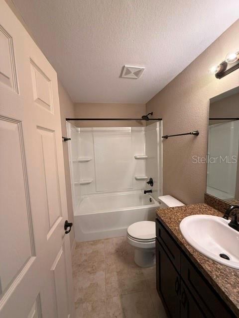 full bathroom with vanity,  shower combination, toilet, and a textured ceiling