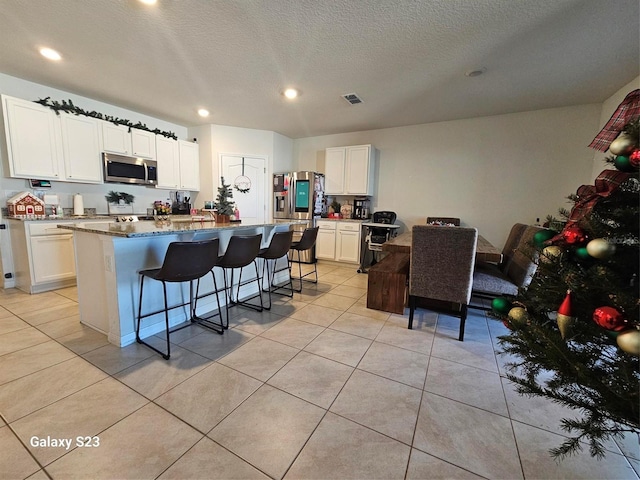 kitchen featuring white cabinetry, dark stone countertops, a kitchen island with sink, a breakfast bar, and appliances with stainless steel finishes