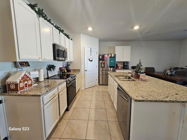 kitchen featuring sink, light stone counters, a center island with sink, white cabinets, and appliances with stainless steel finishes