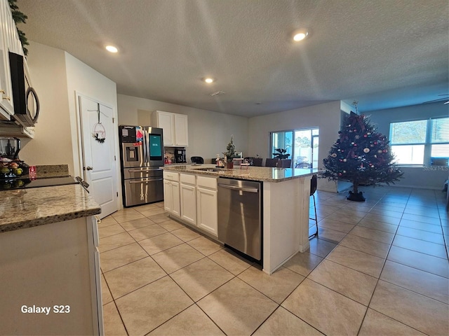 kitchen featuring white cabinets, light stone countertops, stainless steel appliances, and a kitchen island with sink