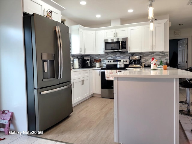 kitchen featuring stainless steel appliances, pendant lighting, a breakfast bar area, decorative backsplash, and white cabinets