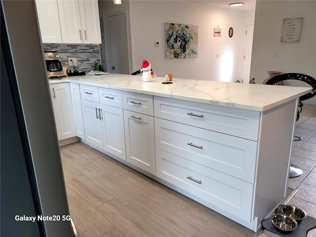 kitchen featuring white cabinets, decorative backsplash, light stone countertops, and kitchen peninsula