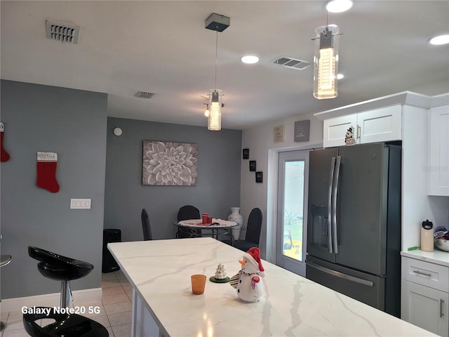 kitchen featuring light stone countertops, white cabinets, pendant lighting, and stainless steel refrigerator with ice dispenser