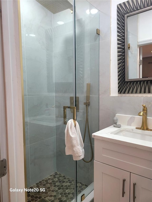 bathroom with vanity, a shower with door, and tile walls