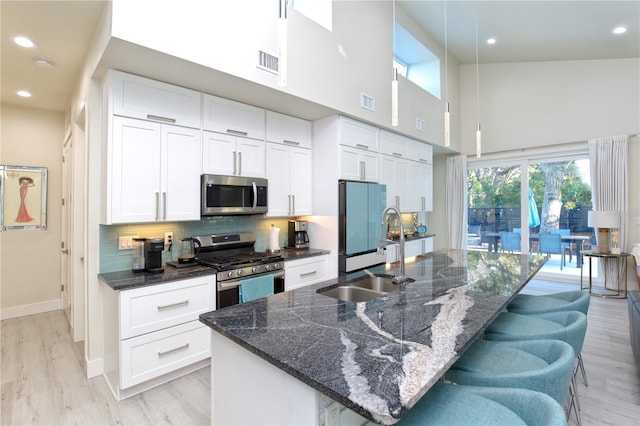 kitchen featuring white cabinets, appliances with stainless steel finishes, a center island with sink, and light hardwood / wood-style flooring