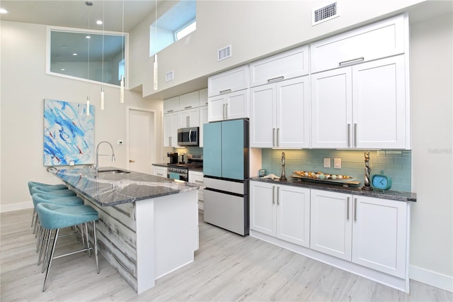 kitchen featuring dark stone counters, a high ceiling, sink, white cabinetry, and stainless steel appliances