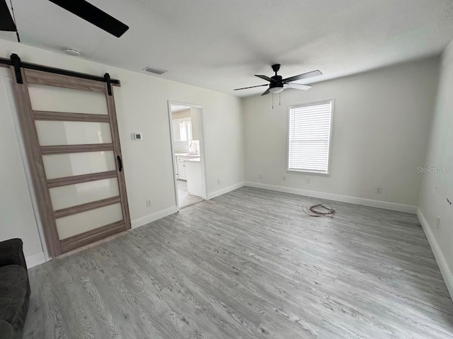 interior space with a barn door, ceiling fan, and light hardwood / wood-style floors