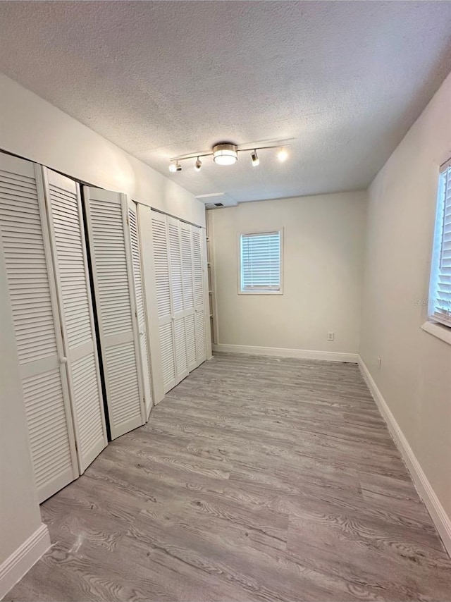 unfurnished bedroom with multiple closets, light hardwood / wood-style flooring, and a textured ceiling