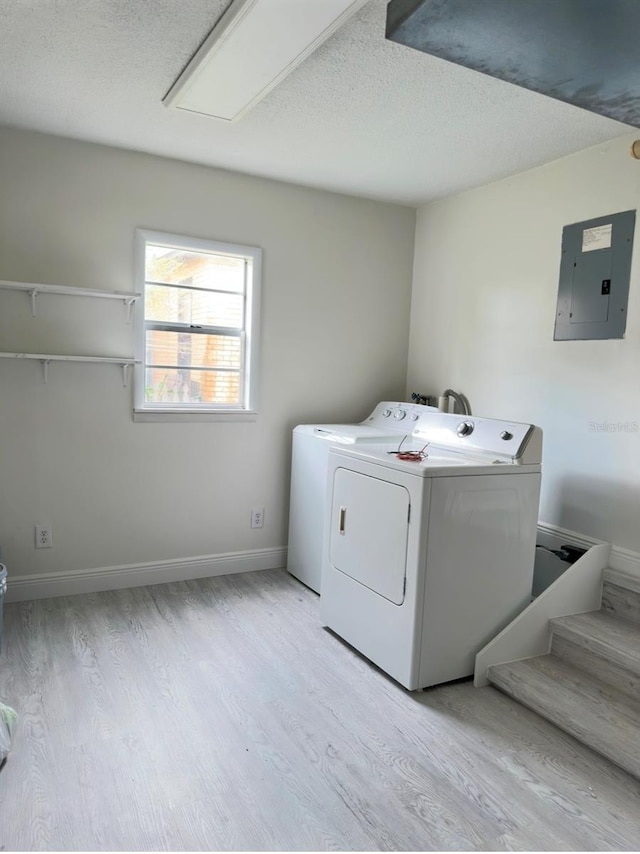 laundry room with electric panel, light hardwood / wood-style floors, a textured ceiling, and independent washer and dryer