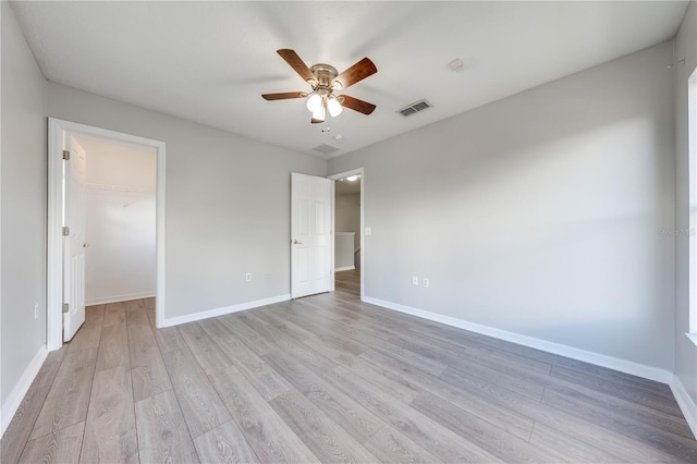 unfurnished bedroom with a closet, a walk in closet, light hardwood / wood-style floors, and ceiling fan