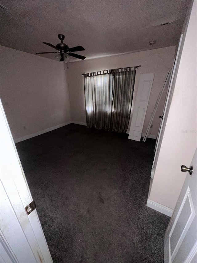 empty room with ceiling fan, dark carpet, and a textured ceiling