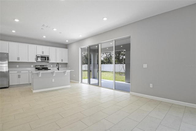 kitchen featuring sink, white cabinetry, stainless steel appliances, a kitchen breakfast bar, and a center island with sink