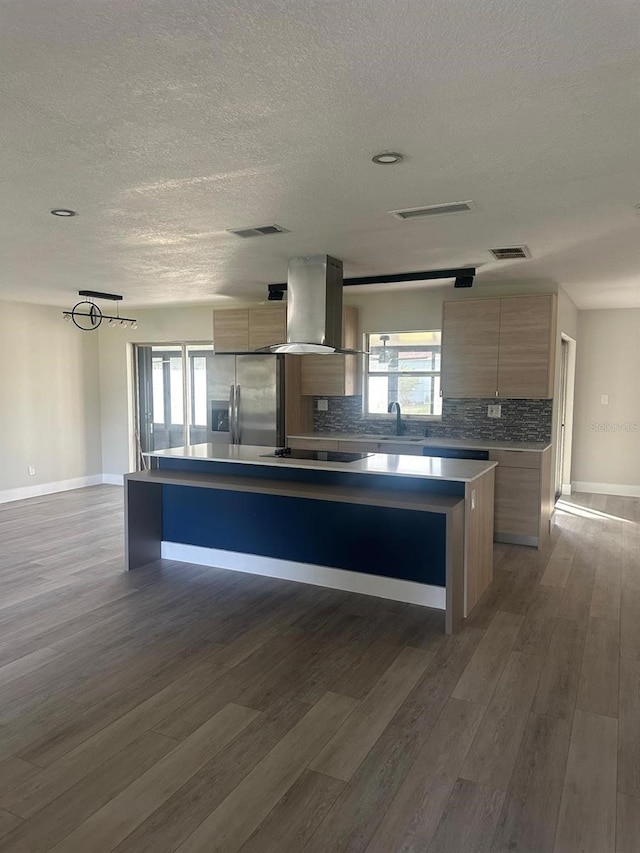 kitchen featuring stainless steel refrigerator with ice dispenser, wall chimney exhaust hood, dark wood-type flooring, sink, and a kitchen island