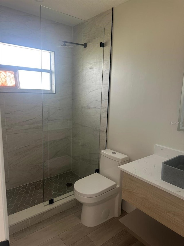 bathroom with tiled shower, wood-type flooring, vanity, and toilet