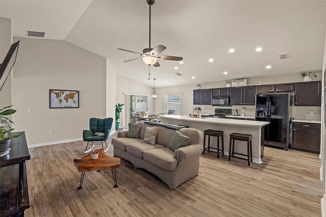 living room featuring light wood-type flooring, vaulted ceiling, ceiling fan, and sink