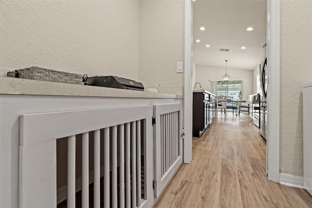 corridor with lofted ceiling, light wood-type flooring, and sink