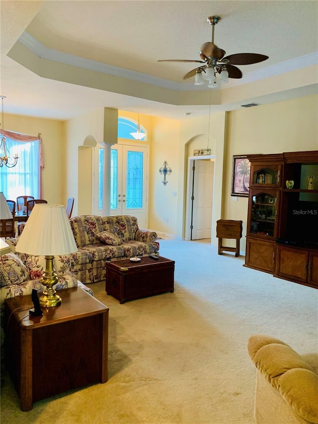 carpeted living room featuring ceiling fan with notable chandelier, ornamental molding, and a raised ceiling