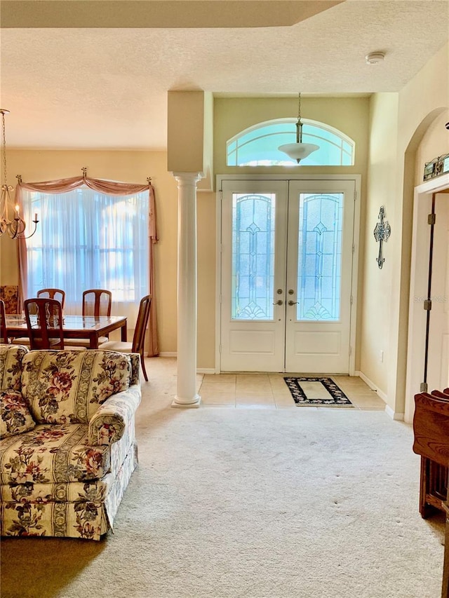 carpeted entrance foyer with ornate columns, french doors, a chandelier, and a textured ceiling