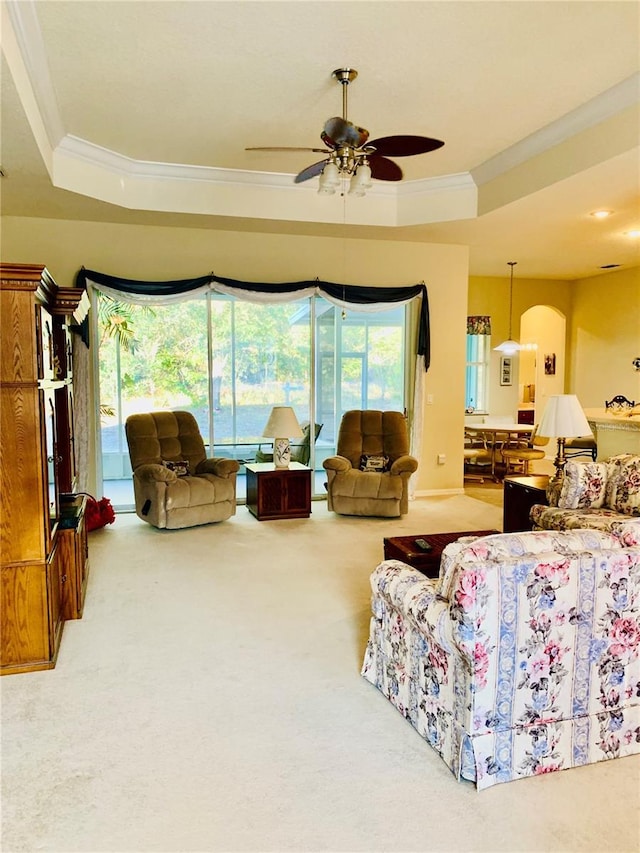 living room featuring carpet floors, ornamental molding, a raised ceiling, and ceiling fan