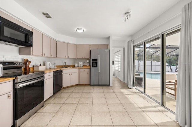 kitchen with backsplash, sink, light tile patterned flooring, and black appliances