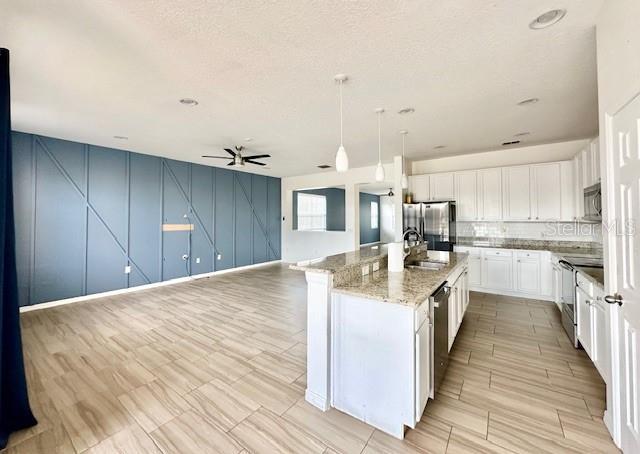 kitchen with ceiling fan, hanging light fixtures, stainless steel appliances, a kitchen island with sink, and white cabinets