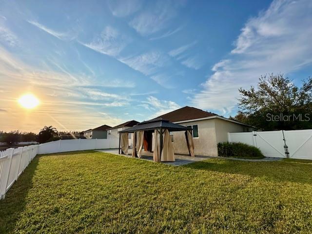 back house at dusk featuring a gazebo and a lawn