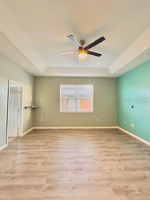 unfurnished room with a tray ceiling, ceiling fan, and light hardwood / wood-style flooring