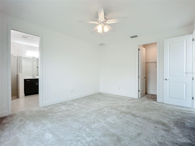 unfurnished bedroom featuring ensuite bath, ceiling fan, light carpet, and a walk in closet