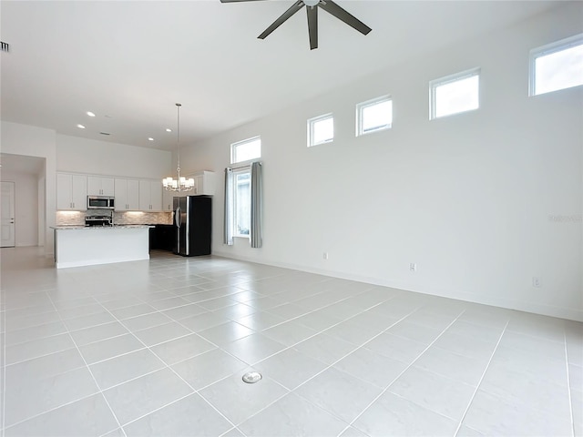 unfurnished living room featuring plenty of natural light, light tile patterned flooring, and ceiling fan with notable chandelier