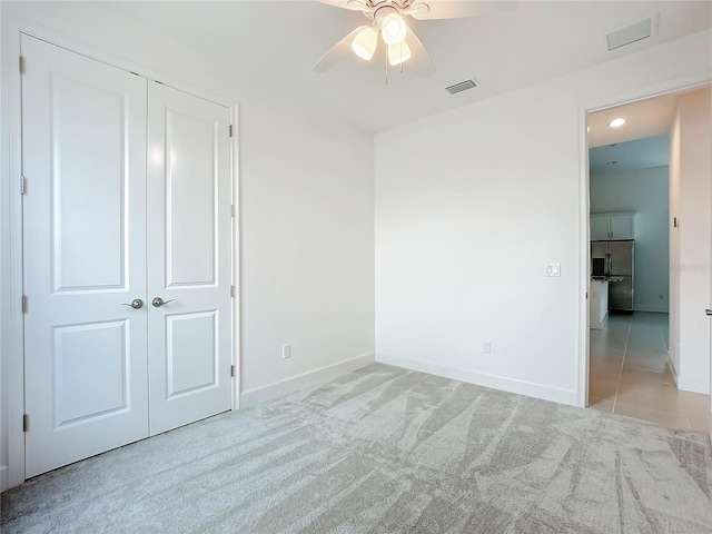 unfurnished bedroom featuring high end refrigerator, a closet, light colored carpet, and ceiling fan