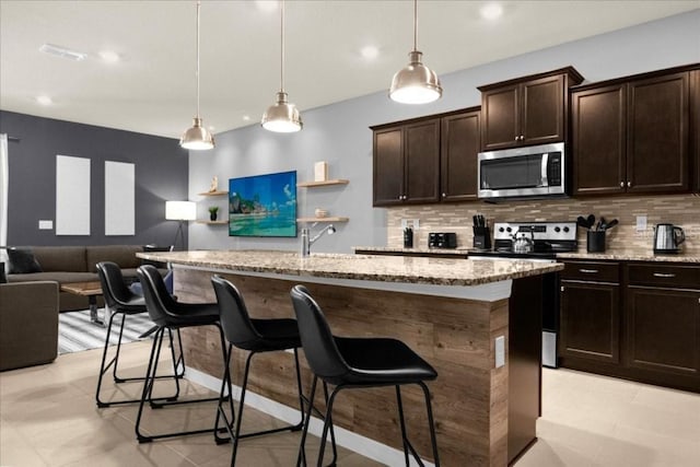 kitchen with a breakfast bar, a center island with sink, pendant lighting, and appliances with stainless steel finishes