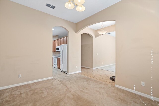 unfurnished room featuring light carpet and a notable chandelier