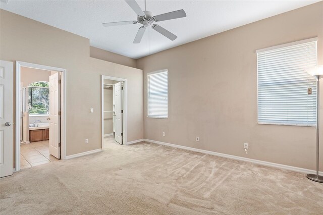 unfurnished bedroom with sink, ensuite bath, a spacious closet, light carpet, and ceiling fan