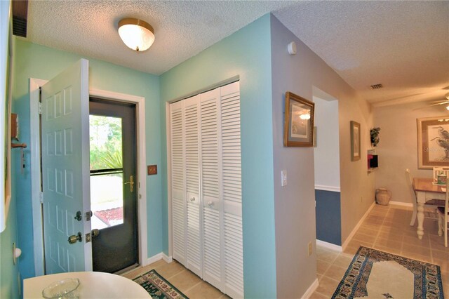 entryway featuring ceiling fan, light tile patterned floors, and a textured ceiling