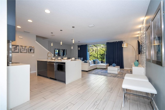 kitchen featuring sink, hanging light fixtures, stainless steel dishwasher, and light wood-type flooring