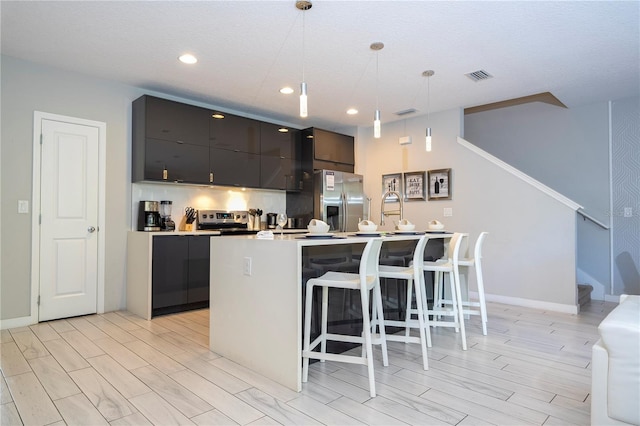 kitchen featuring light wood-type flooring, stainless steel appliances, pendant lighting, a breakfast bar area, and an island with sink